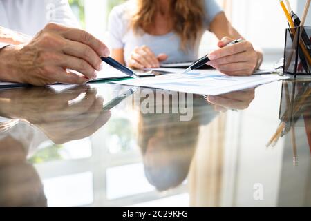 Mid- Section Of Two Businesspeople Analyzing Graph Over Office Desk Stock Photo