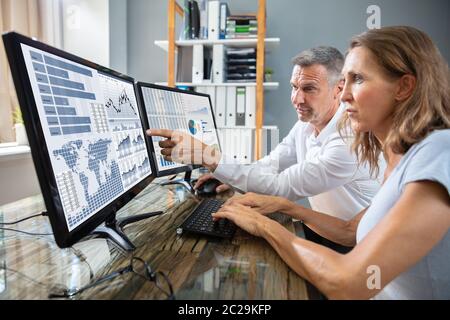 Side View Of Male And Female Stock Market Broker Analyzing Graphs On Laptop At Workplace Stock Photo