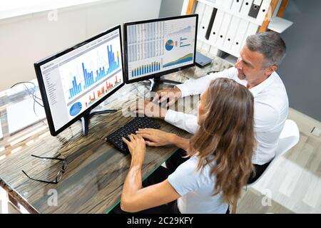 Side View Of Male And Female Stock Market Broker Analyzing Graphs On Laptop At Workplace Stock Photo