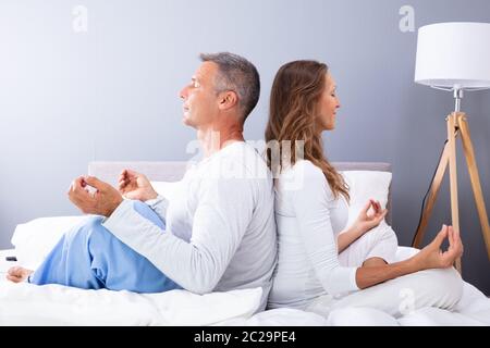 Matured Couple Sitting Back To Back On Bed Meditating Stock Photo