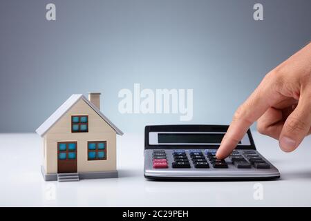 Person's Hand Calculating With Calculator Near House Model On Desk Stock Photo