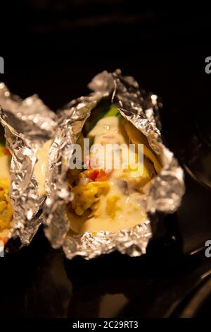 Avocado and egg burritos in corn tortillas, topped with creamy queso sauce and wrapped in foil Stock Photo