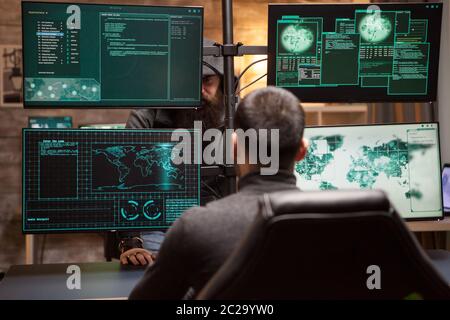 Bearded old hacker wearing a hoodie talking with young hacker about new cyber attack. Stock Photo