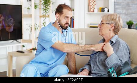 Male doctor putting his stethoscope on and listening old woman heartbeat in nursing home Stock Photo