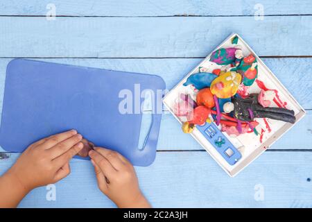 children's hands sculpt figures of clay on a blue table. the view from the top Stock Photo