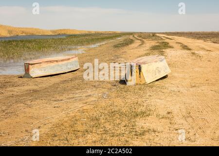 A boat turned upside down. Rowing boats in the reeds. Wooden boat on a grassy lake shore on a summer