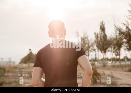 portrait of a young Caucasian guy in a black t-shirt and black shorts running over rough terrain during sunset Stock Photo