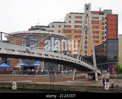 the millennium footbridge in leeds with people drinking at an outside bar after work and men fishing in the river Stock Photo