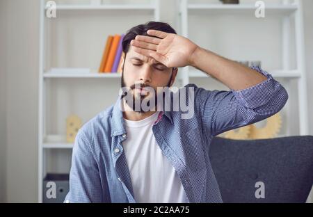 Young bearded man with closed eyes have headache touching forehead with back of his palm. Front view Stock Photo