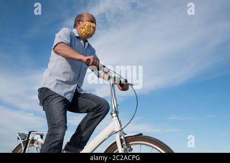 Mature man in mask riding on bicycle outdoor. Stock Photo