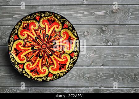 Decorative ceramic plate, hand painted with acrylic paints on a wooden background. Closeup with place for text. Stock Photo