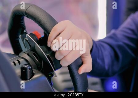 Man gamer hand using black gaming steering wheel joystick and playing in car drive simulator at modern technology exhibition. Entertainment, hobby Stock Photo