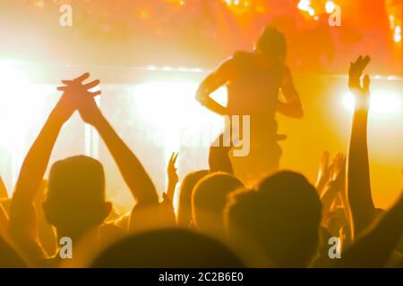 People crowd partying, cheering, raising hands up and clapping at rock concert in front of stage of nightclub. Bright stage lighting. Nightlife and Stock Photo