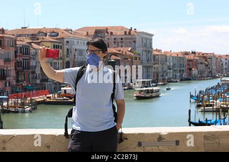 young man with surgical mask takes a selfie on the Rialto bridge in Venice in Italy during the emergency from Corona Virus Stock Photo