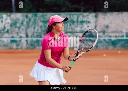 Tennis player. Attractive young woman playing tennis and waiting for the serve. Dressed in t-sport shirt and skirt. Outdoors. Stock Photo