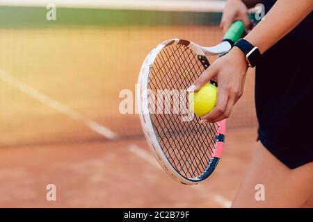 Tennis player. Close-up view of female hands holding racket and ball, preparing to serve, playing tennis on the court. Stock Photo