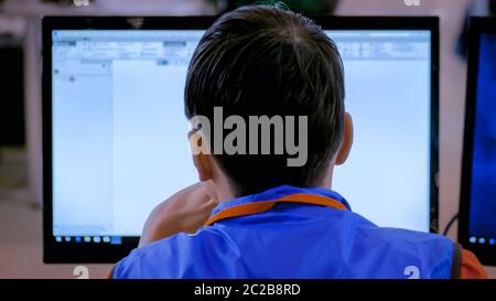 Back view - professional young male architect looking at display and working with blueprint on computer at office - close up. Work, architecture and Stock Photo