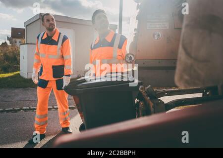 Garbage removal men working for a public utility emptying trash container Stock Photo