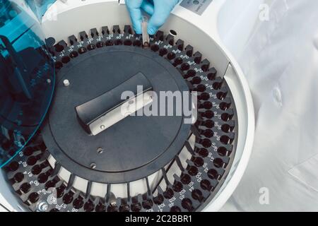 Lab technician loading centrifuge with tubes of human blood to analyze it Stock Photo