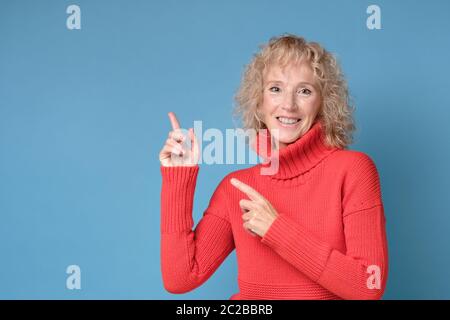 Woman smiling cheerfully and pointing with forefingers aside Stock Photo