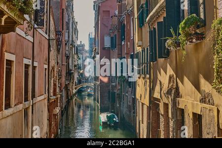 A picturesque venetian canal, with the colourful historic houses, a pedestrian bridge and boats moored, on a sunny winter day Stock Photo
