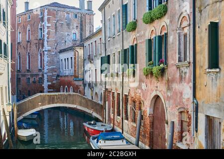 A picturesque view of a Venetian canal, with the colourful historic houses overlooking it, a pedestrian bridge and boats moored, on a sunny winter day Stock Photo