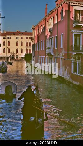 A typical Venetian canal that flows through the colourful historic houses, with a gondola and its gondolier in the foreground, on a sunny winter day Stock Photo