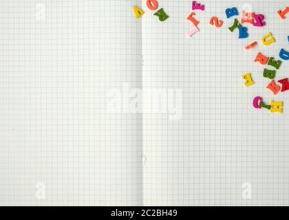 open notebook with white sheets in a box and small multi-colored wooden letters, back to school, copy space Stock Photo