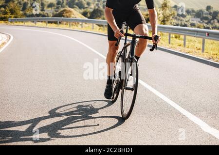 Close up of mature man with strong body wearing cycling clothing and sneakers, riding bike on countryside. Concept of active lifestyle and regular tra Stock Photo