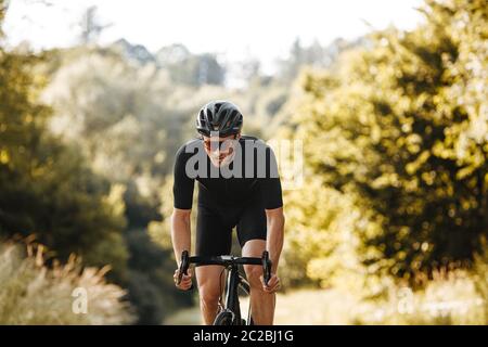 Portrait of mature bearded man in cycling outfit, protective helmet and glasses biking among green forest. Concept of training on  nature. Stock Photo