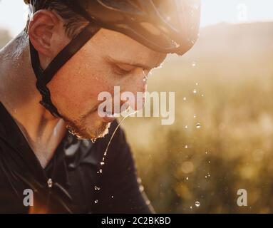 Close up portrait of tired bearded athlete in protective helmet with water drops on his face. Mature man splashed water to refresh after hard training Stock Photo
