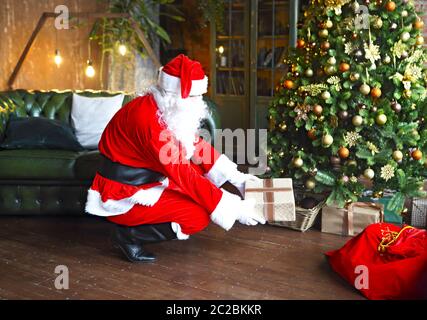 Santa Claus secretly putting gift boxes under the Christmas tree Stock Photo