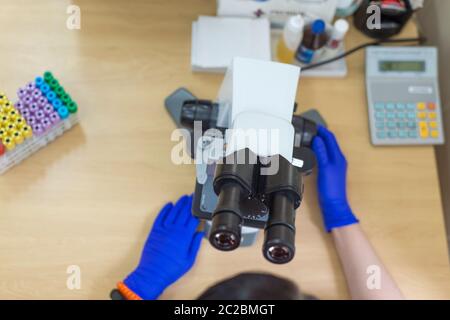Scientist conducting research taking notes whilst looking through microscope selective focus laboratory assistant is looking through a microscope. Clo Stock Photo