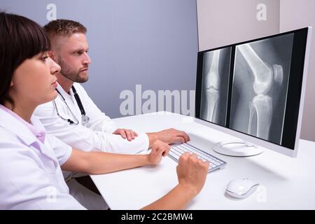 Doctors Examining Knee X-ray On Computer In Clinic Stock Photo