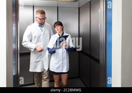 Male Doctor Discussing Over Medical Report With Nurse Standing In The Elevator At Hospital Stock Photo