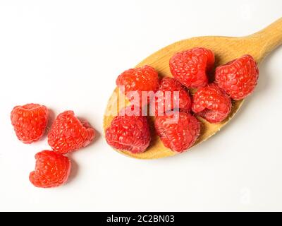 Fresh raspberries on a wooden spoon with three raspberries spilling over on a white background Stock Photo
