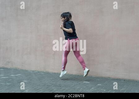 portrait of a young indian runner, athlete jumping on a texture wall background. Active street lifestyle, workout, jumping, girl doing sport exercises Stock Photo