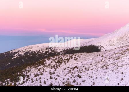 Sunset in mountains. Winter scenery. Beautiful pink and white sky, windy weather. Pink, purple and blue mild pastel colors Stock Photo