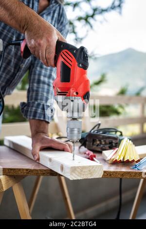 Adult craftsman carpenter with electric drill works makes a hole on a wooden table. Housework do it yourself. Stock photography. Stock Photo