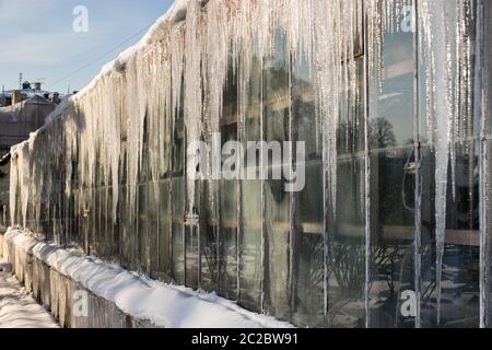 Sharp icicles on the roof of the greenhouse in sunny winter day on the sunny side, horizontal. Formation of icicles in a thaw. Icicles hanging down fr Stock Photo