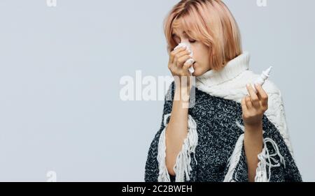 Studio portrait of cute unhealthy Caucasian woman with paper napkin sneezing, using nasal spray to help herself, experiences allergy symptoms, caught Stock Photo