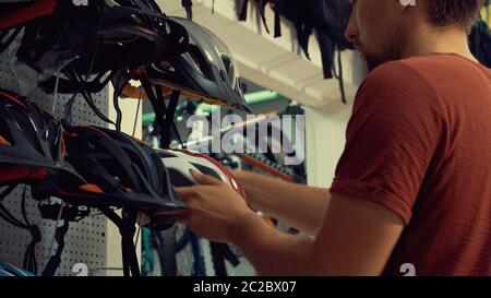 A young Caucasian man stands near a stand in a bicycle store in the head protection department. Choosing a bicycle helmet in a s Stock Photo