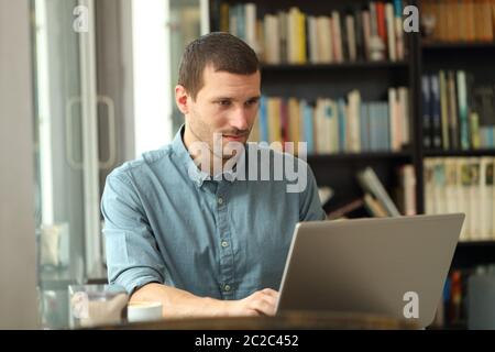 Serious adult man writing on laptop entering data sitting in a coffee shop or home Stock Photo