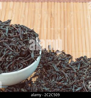 Dried tea is poured into a ceramic cup on a bamboo mat Stock Photo
