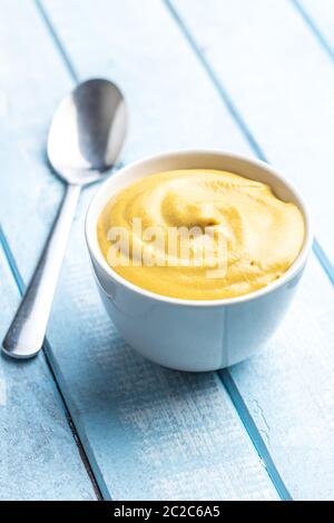 Yellow mustard in bowl on blue table. Stock Photo