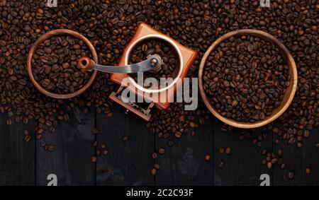 Ground coffee, coffee mill, bowl of roasted coffee beans on black wooden background, top view