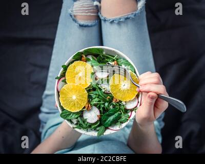 Woman in jeans at bed, holding vegan salad bowl Stock Photo