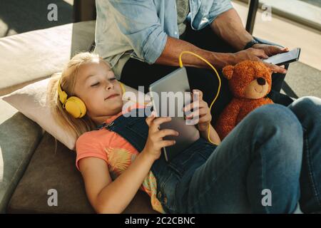Girl using tablet pc with her father sitting on side with a mobile phone at airport waiting lounge. Family relaxing at airport waiting lounge. Stock Photo
