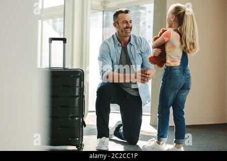 Daughter holding a teddybear greets her father at the entrance door when he arrives back from a business trip. Daughter talking with her father just a Stock Photo