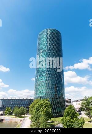 westhafen tower in frankfurt am main with trees in the front on a cloudy day